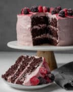 A slice of cake on a small plate with the whole cake on a stand in background.