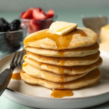 close-up stack of fluffy vegan pancakes with vegan butter and maple syrup.