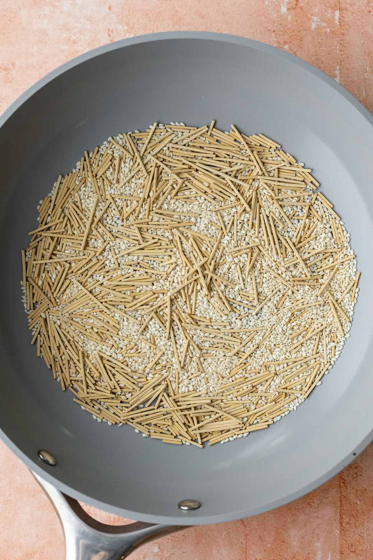 Toasting broken ramen noodles and sesame seeds in a pan.