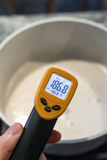 Using a thermometer to check the temperature of the oat creamer mixture.