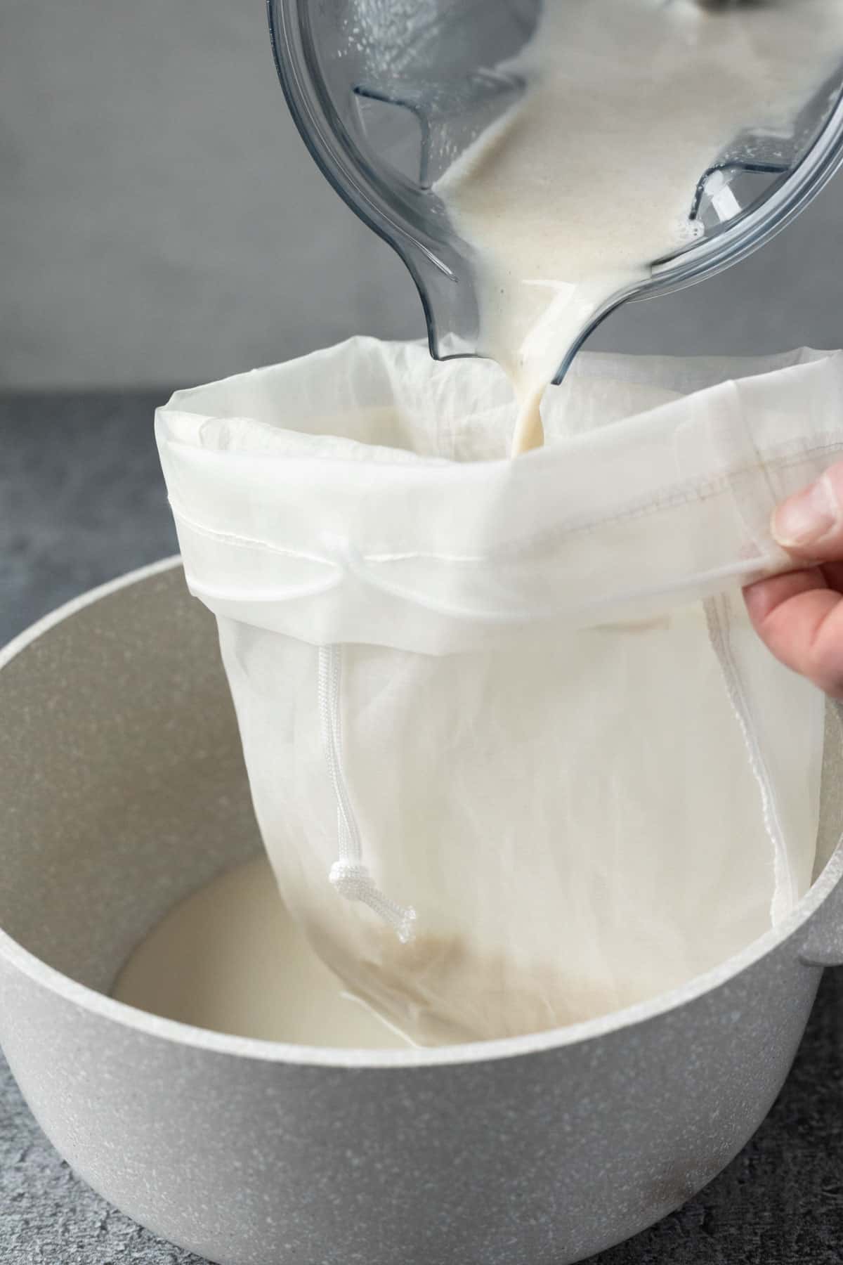 Pouring the oat milk through a nut milk bag.