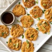 Assortment of baked and fried vermicelli noodle pancakes on a baking sheet with a bowl of Asian dipping sauce.