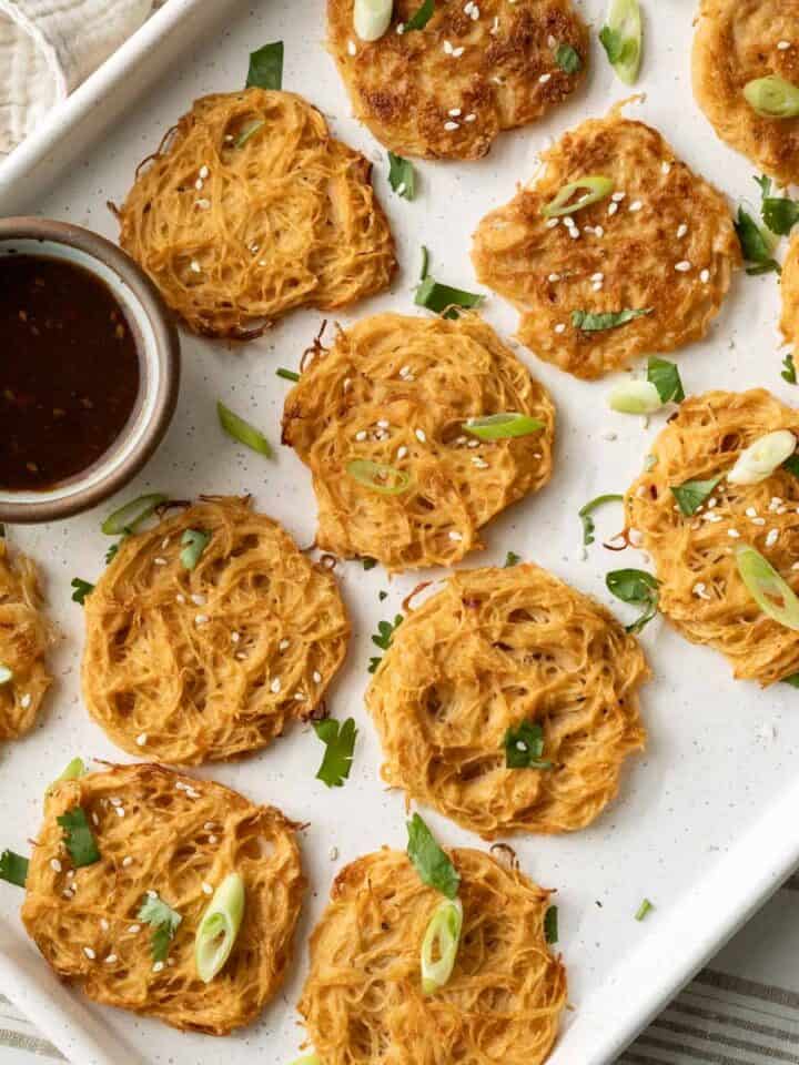 Assortment of baked and fried vermicelli noodle pancakes on a baking sheet with a bowl of Asian dipping sauce.