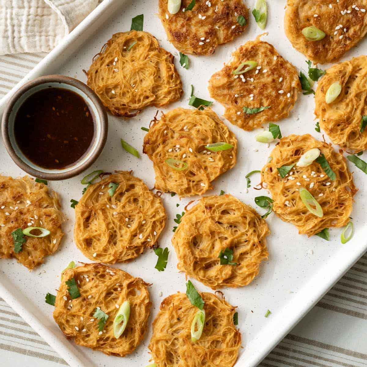 Assortment of baked and fried vermicelli noodle pancakes on a baking sheet with a bowl of Asian dipping sauce.