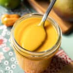 close-up of mango habanero sauce in a glass jar with a spoon scooping some out.
