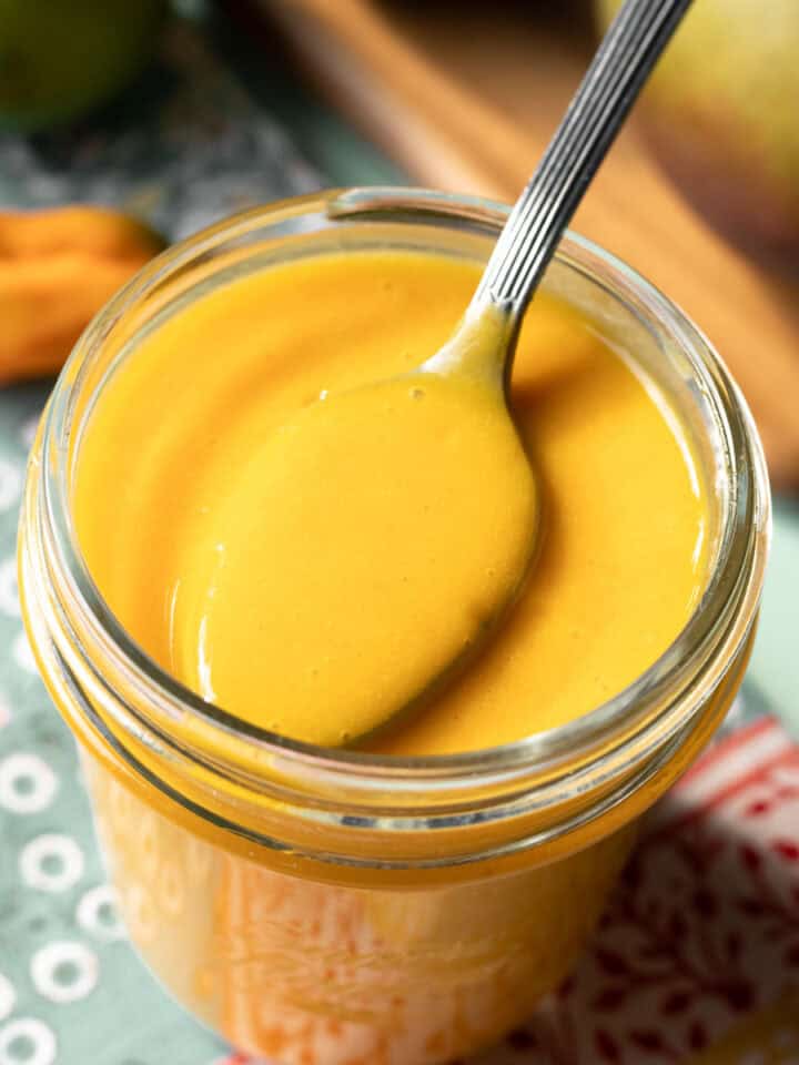 close-up of mango habanero sauce in a glass jar with a spoon scooping some out.