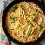 Cast iron skillet filled with pan-fried tofu in creamy corn with tomatoes and basil.