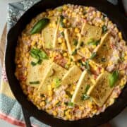 Cast iron skillet filled with pan-fried tofu in creamy corn with tomatoes and basil.
