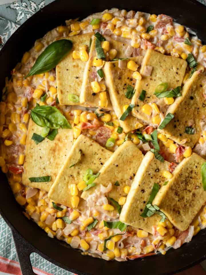 Cast iron skillet filled with pan-fried tofu in creamy corn with tomatoes and basil.