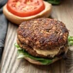 Two thick homemade veggie burgers stacked on a bun with mustard, lettuce, and tomato.