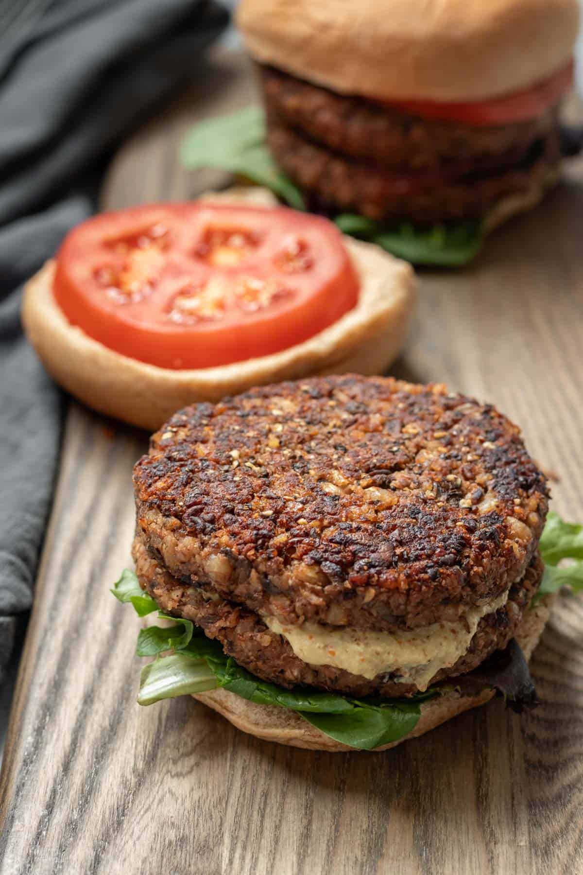 Open-face veggie burger with bun and tomato in background.