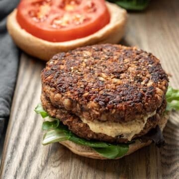 Two thick homemade veggie burgers stacked on a bun with mustard, lettuce, and tomato.