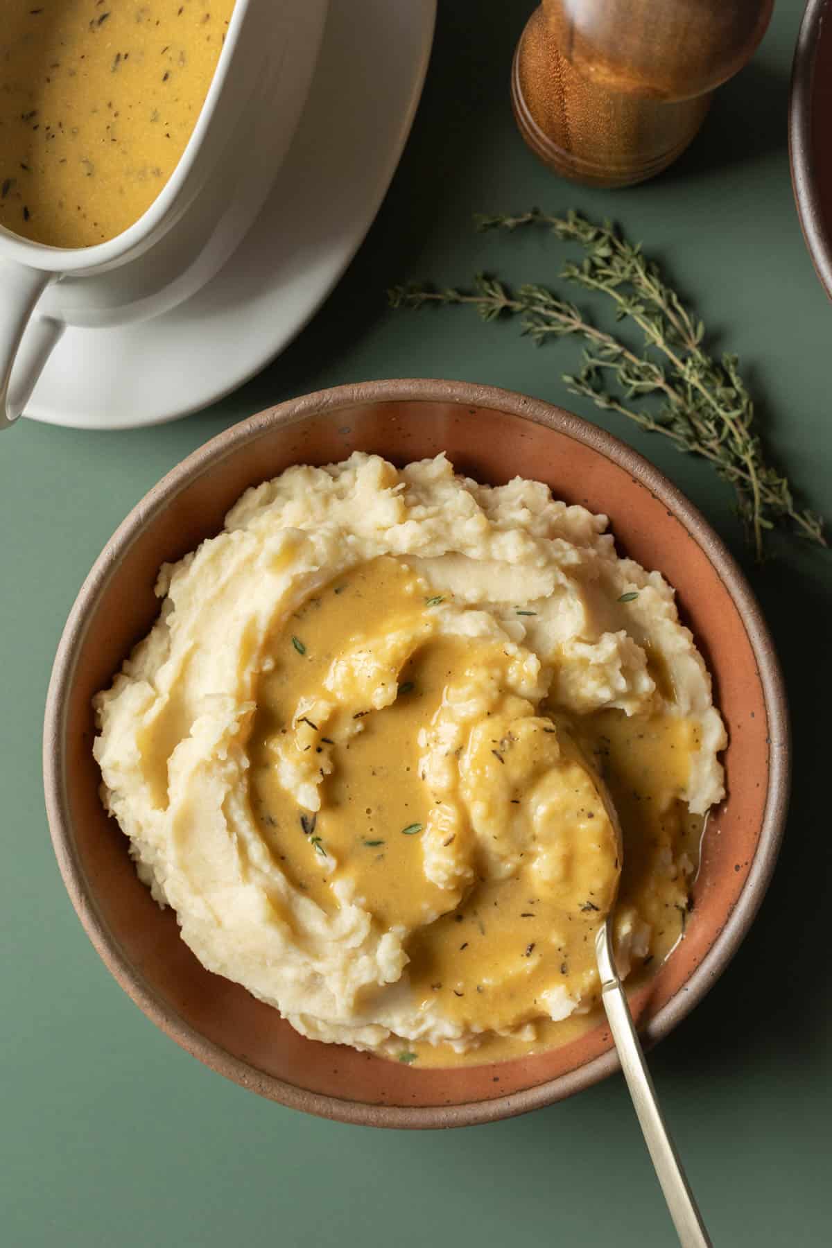 A bowl full of mashed potatoes topped with vegan brown gravy with a gravy boat nearby.