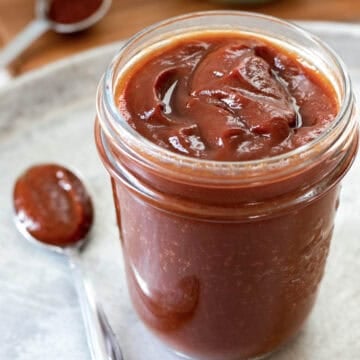 Thick homemade bbq sauce in a glass jar with a spoonful nearby.