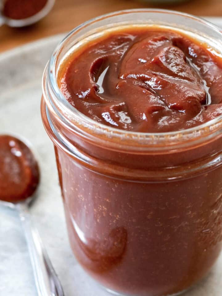 Thick homemade bbq sauce in a glass jar with a spoonful nearby.