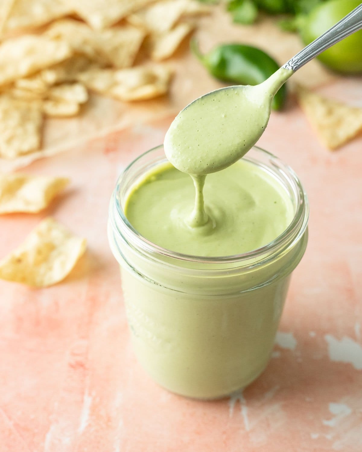 A glass jar filled with creamy fresh jalapeno dressing with tortilla chips in the background.