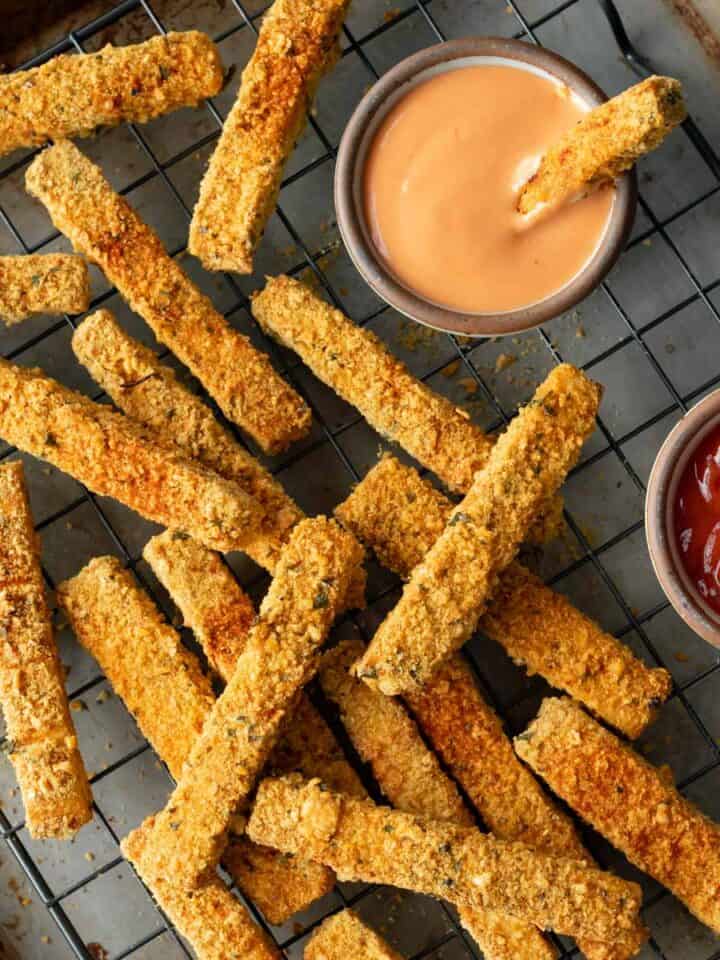 close-up overhead of tofu fries after baking on a wire rack with dipping sauces on the side.