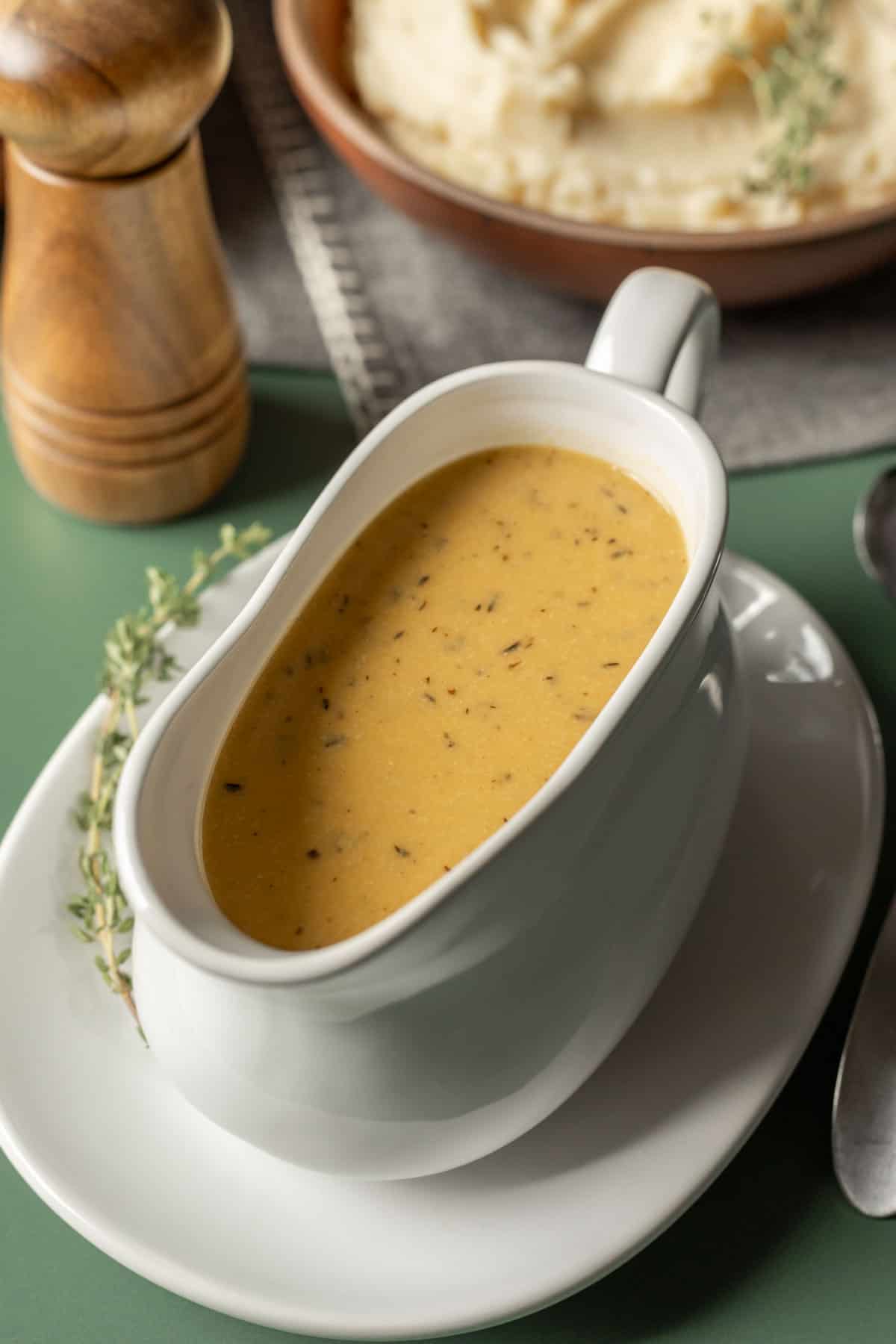 A white gravy boat filled with vegan gravy with sprigs of thyme on the plate.