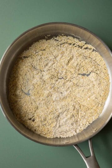 Toasting oat flour, thyme, and nutritional yeast in a pan.