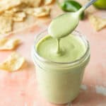 A spoon drizzling creamy jalapeno dressing in a glass jar.