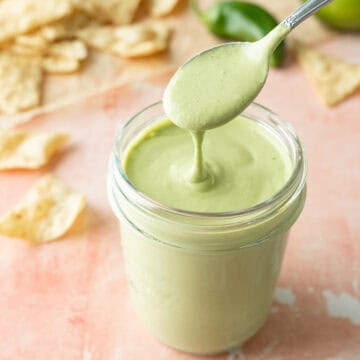 A spoon drizzling creamy jalapeno dressing in a glass jar.