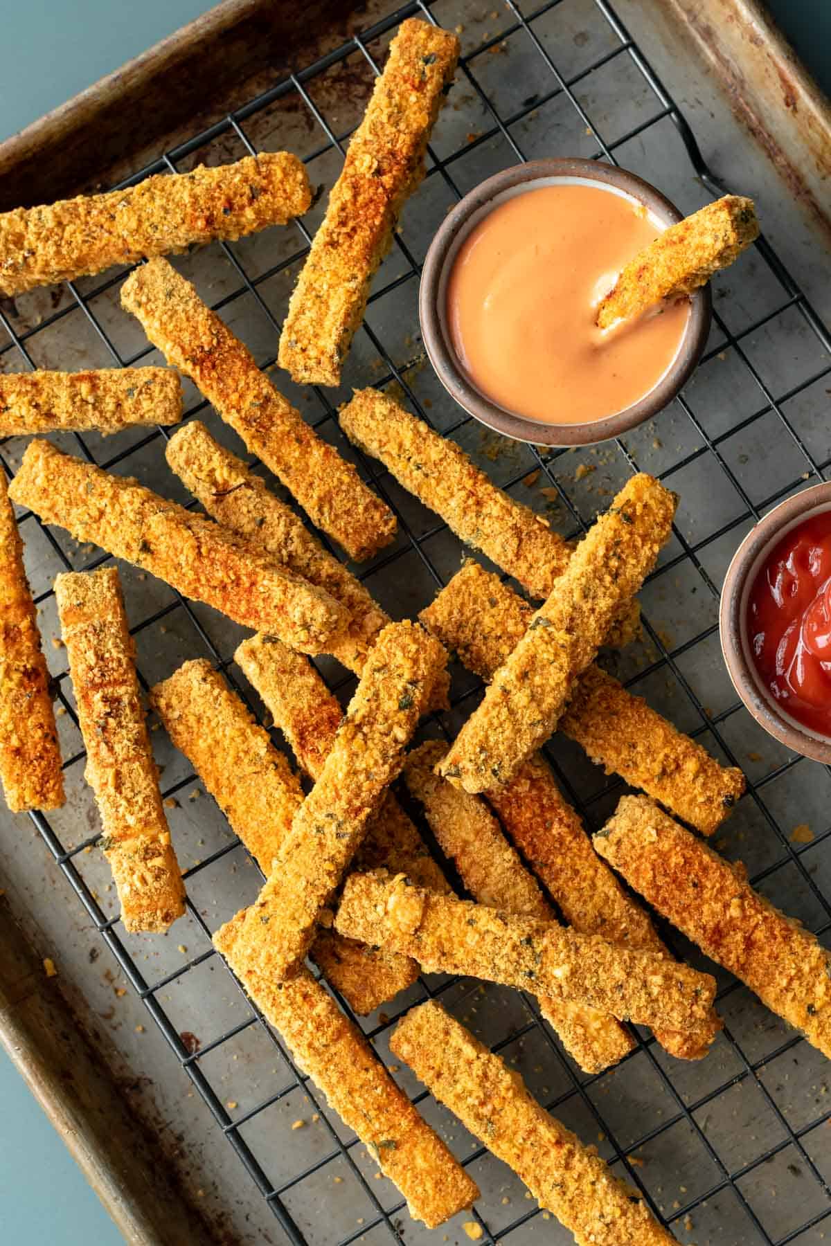 tofu fries on a wire rack after baking with dipping sauces on the side.