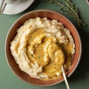 Gravy made with olive oil drizzled on a bowl of mashed potatoes against a dark gren background.