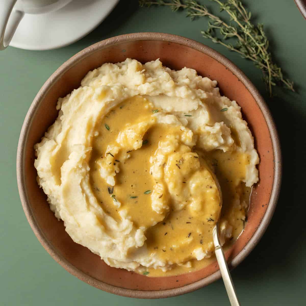 Gravy made with olive oil drizzled on a bowl of mashed potatoes against a dark gren background.