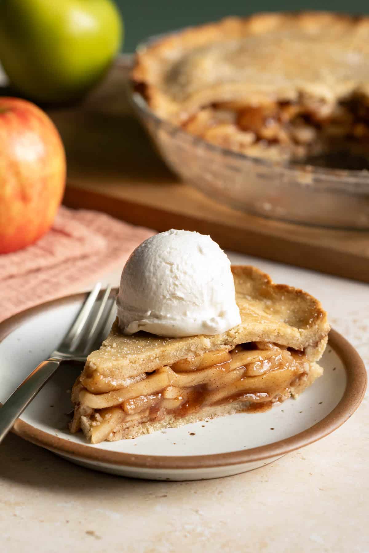 A slice of vegan apple pie on a plate made with gluten free almond flour crust and topped with a scoop of ice cream.