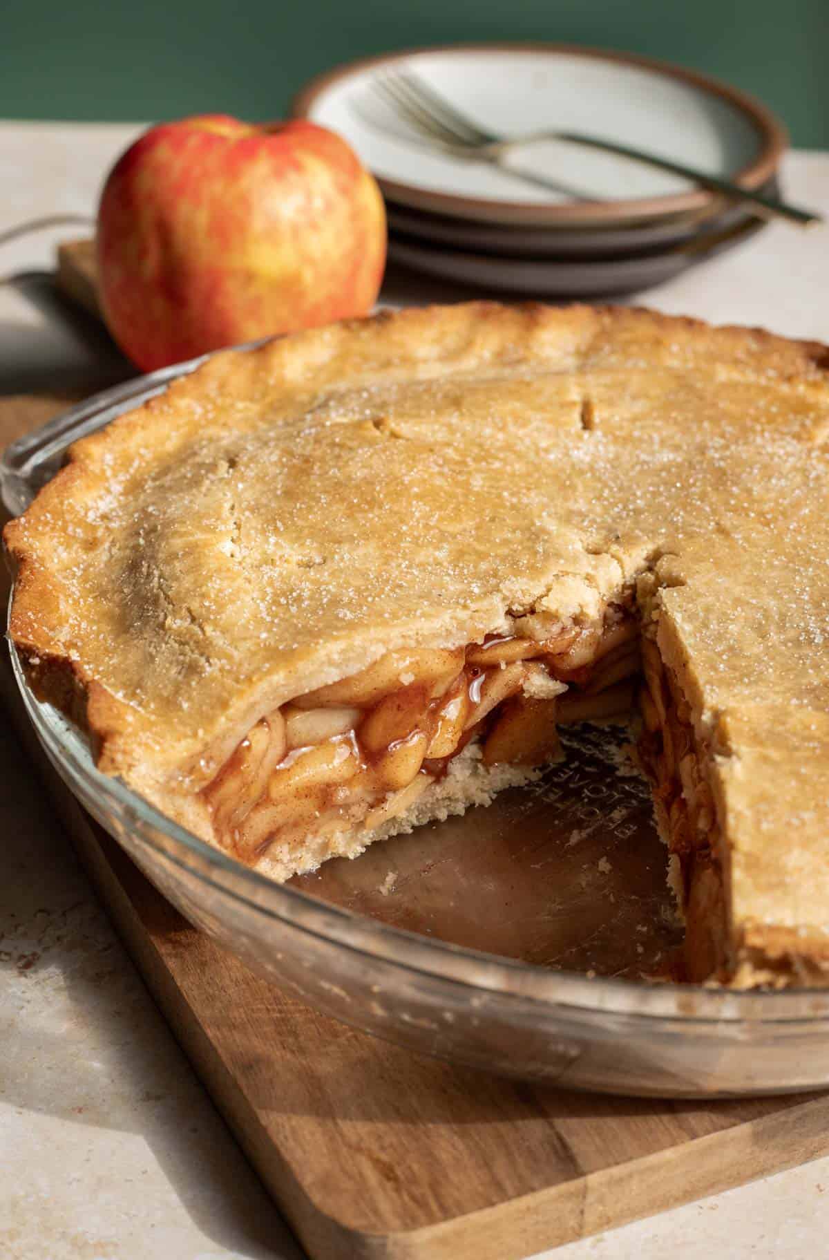 A whole apple pie in a pie plate with a large slice removed to show the apple filling inside.