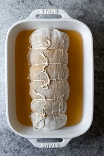 Large vegan roast wrapped in cheesecloth, tied and resting in a baking dish.