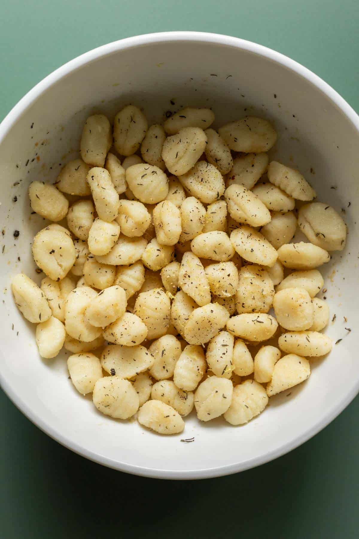 Tossing gnocchi with seasonings in a large bowl.