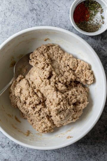 Stirring together the seitan dough in a large bowl with herb rub nearby.