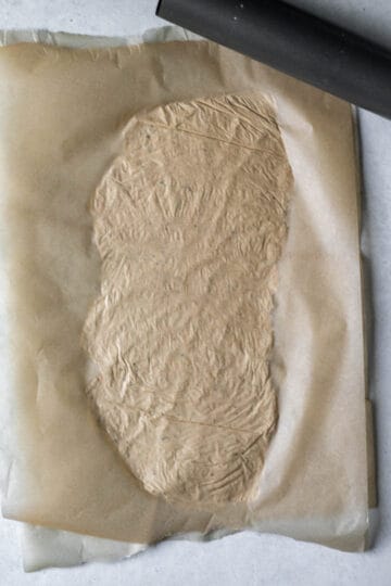 Rolling out whole wheat cracker dough between two pieces of parchment paper.