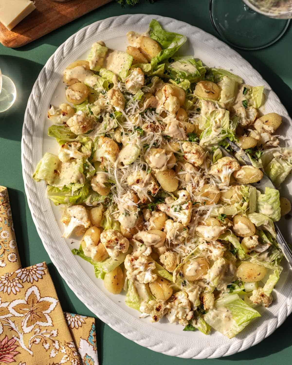 A serving platter filled with roasted gnocchi Caesar salad on a green background.