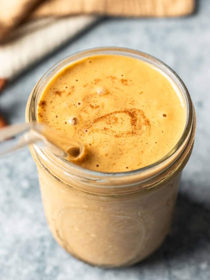 A creamy orange-colored sweet potato smoothie in a glass sprinkled with cinnamon.