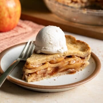 A slice of vegan apple pie topped with a scoop of vanilla ice cream on a small plate.