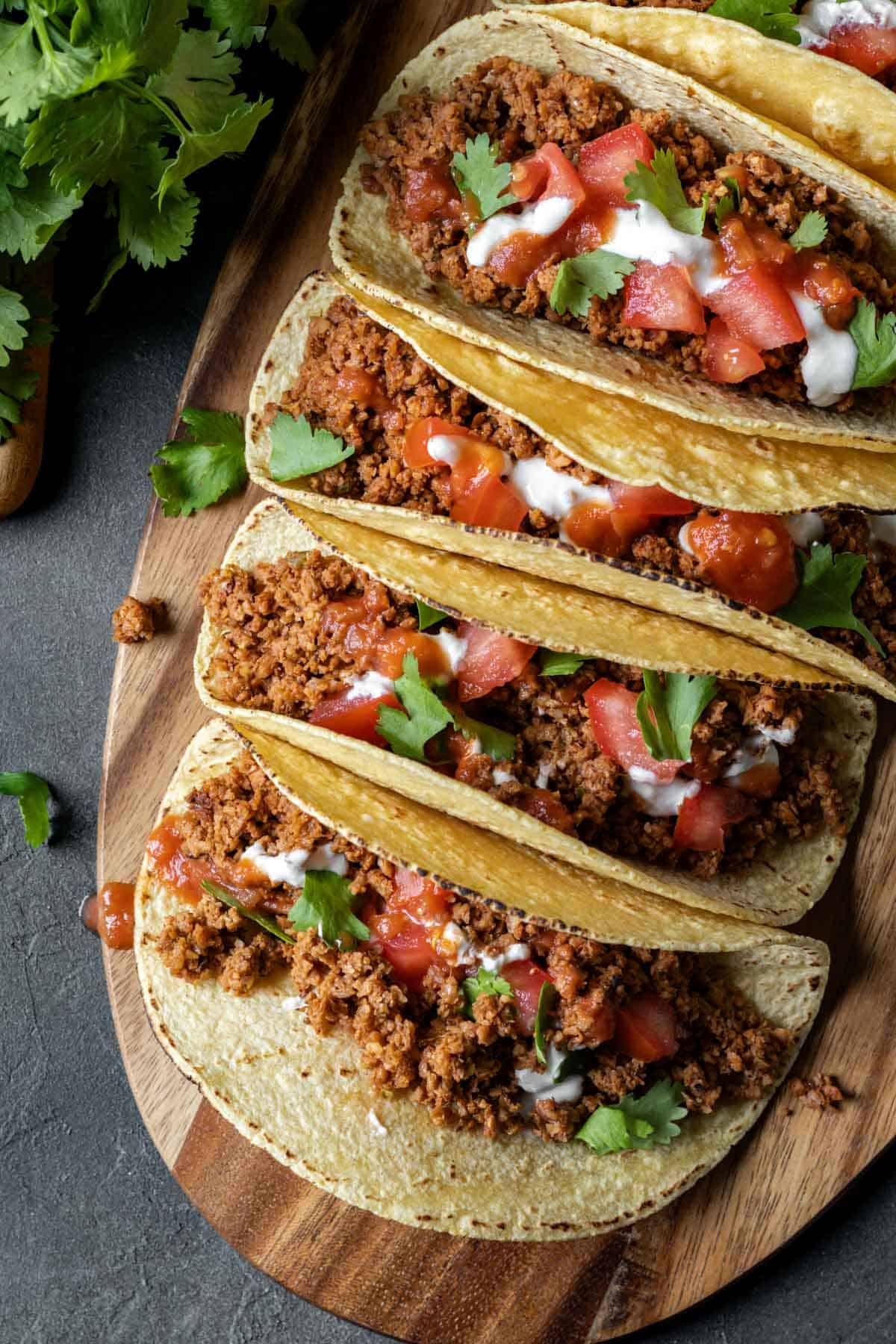 Vegan tacos lined up on a wood serving board.