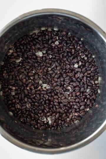 Black beans in a pressure cooker with onion, garlic, and seasonings.