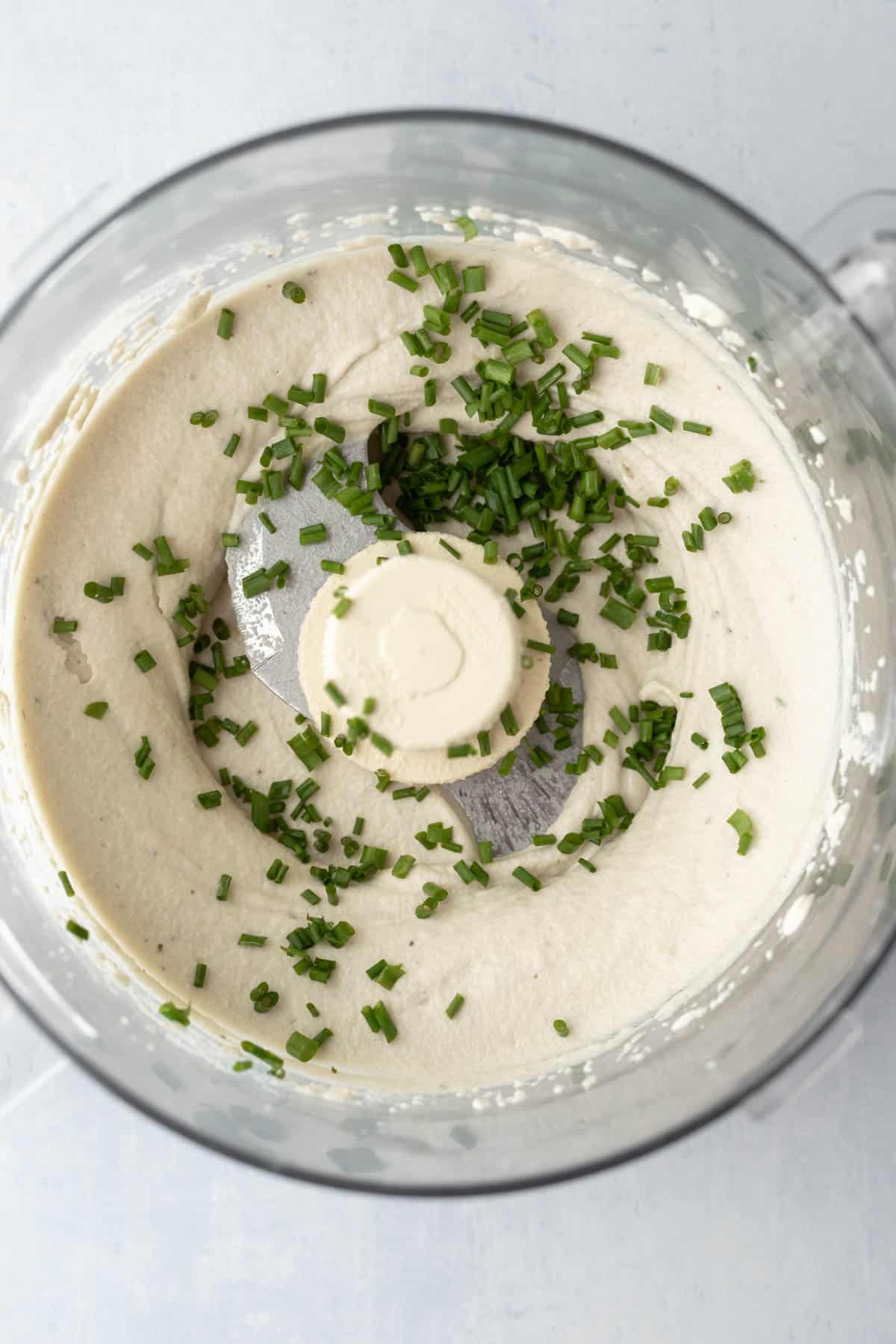 Creamy cashew boursin inside a food processor with fresh chopped chives.