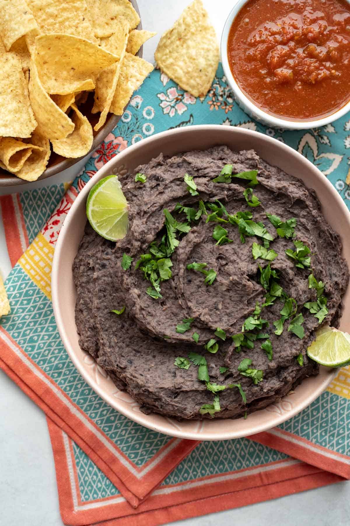 Refried beans in a bowl garnished with cilantro and lime wedges.