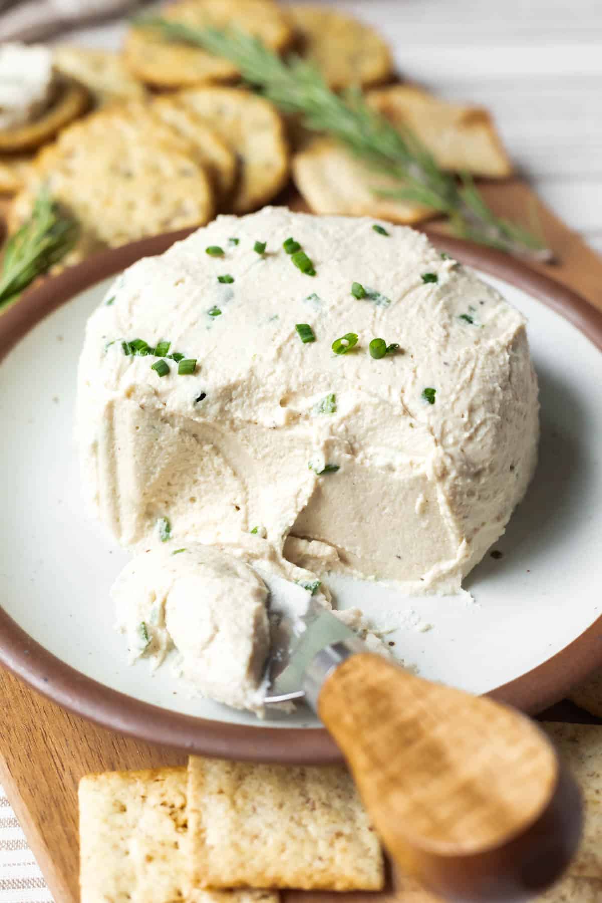 A wheel of homemade vegan Boursin cheese on a board surrounded by crackers.