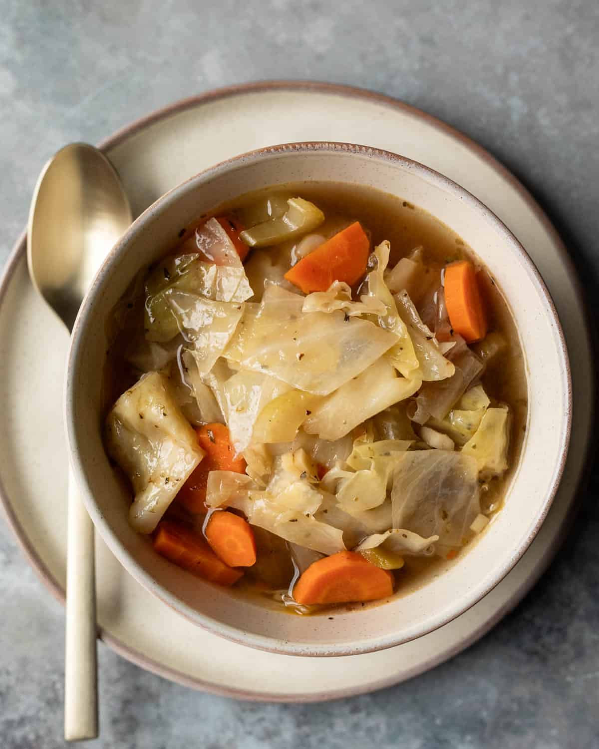 A bowl of crockpot cabbage soup sitting on a plate with a spoon.