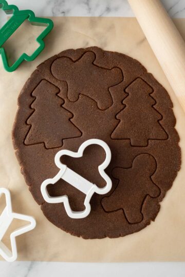 Cutting shapes in gingerbread cookie dough with cookie cutters.