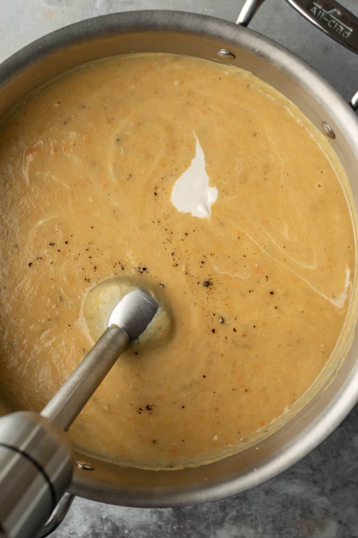 Using an immersion blender to blend the gold potato soup in a pot.