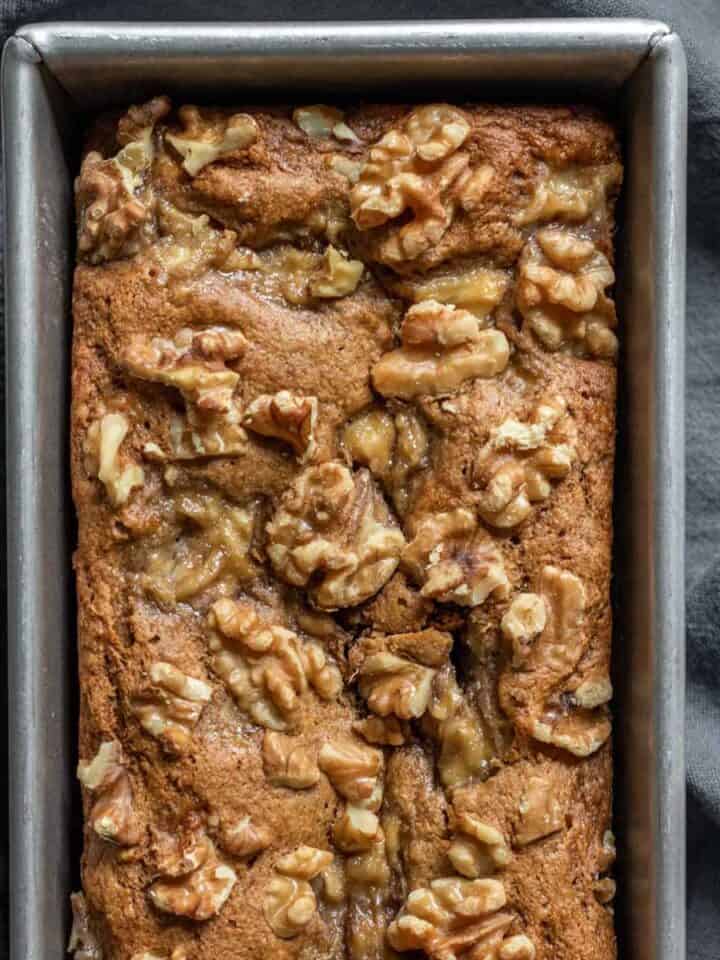 Freshly baked banana bread topped with walnuts against a dark background.