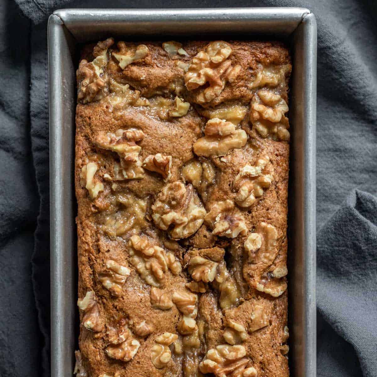 Freshly baked banana bread topped with walnuts against a dark background.