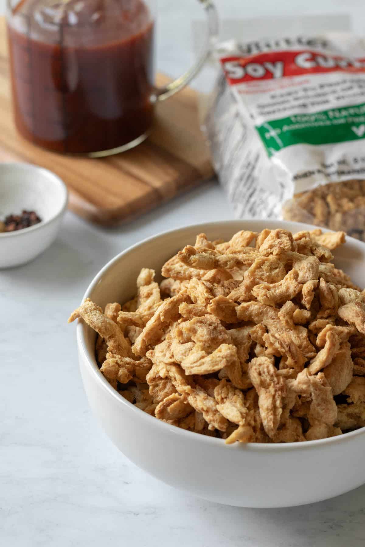 dry soy curls in a bowl with barbecue sauce in background.