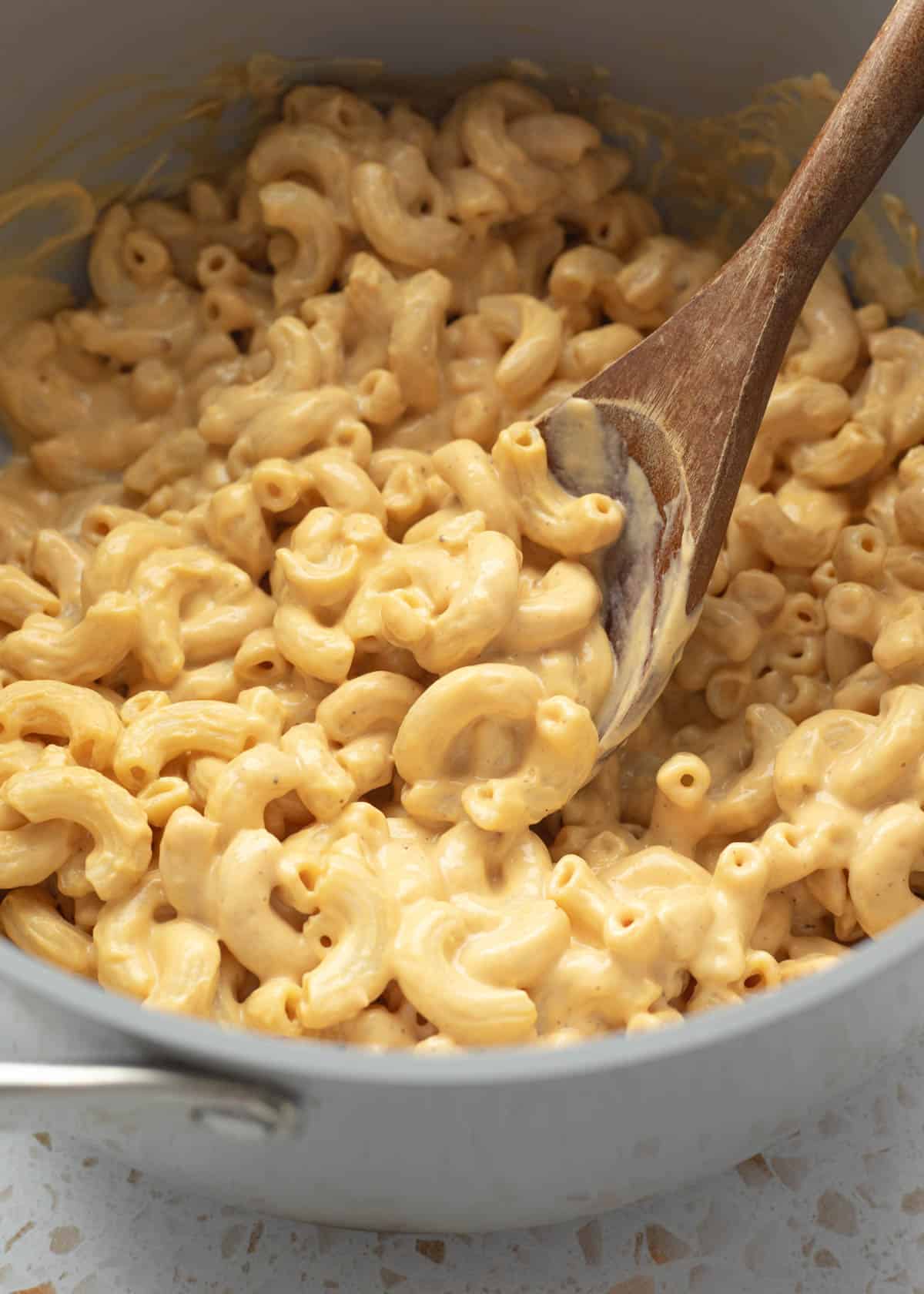 Scooping up macaroni coated in cheesy silken tofu sauce from a large pot.