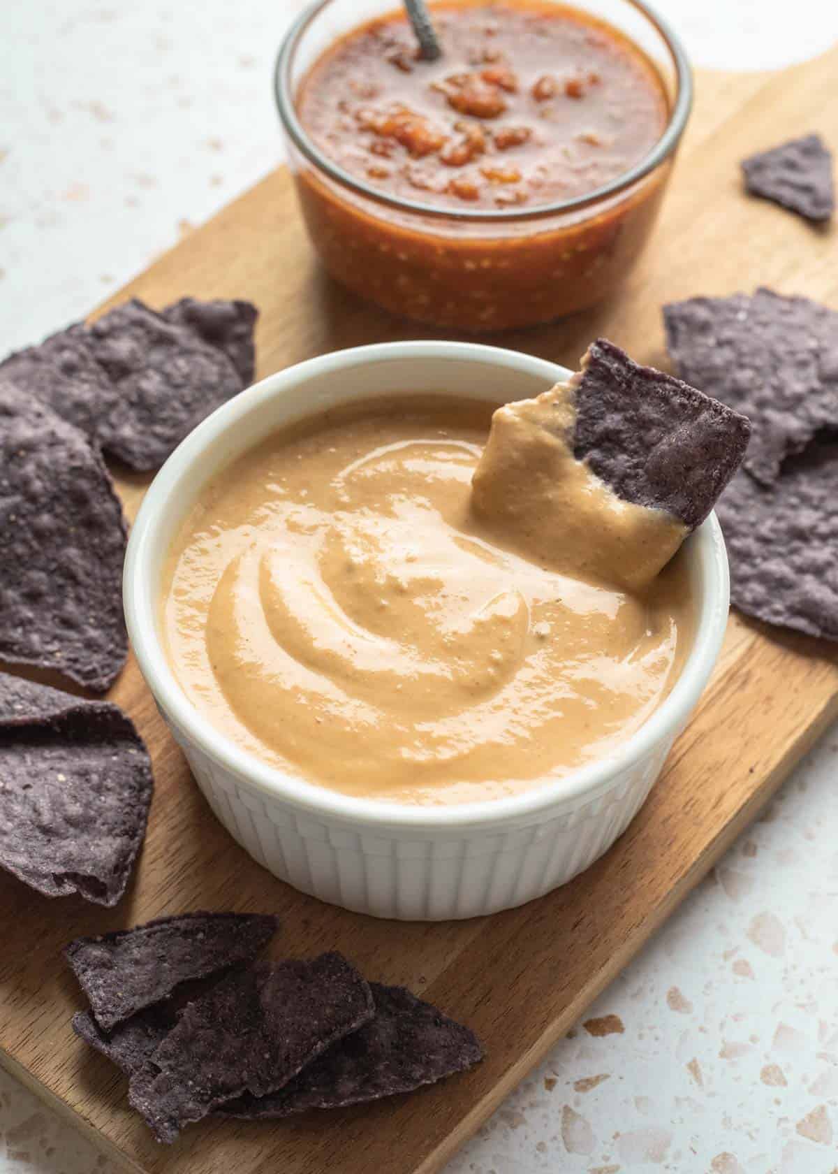 Tofu queso dip in a white bowl with a blue corn tortilla chip in it and more around it.